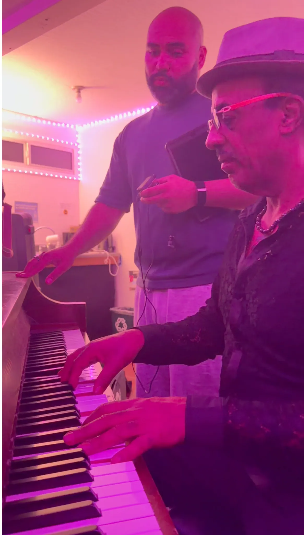 Two Guajirón musicians working together at a piano under magenta studio lighting